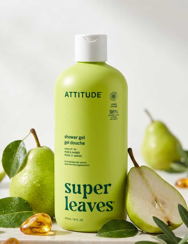 A bottle of ATTITUDE shower gel in the Super Leaves scent, styled with fresh green pears, leaves, and a honeycomb lid on a light background.